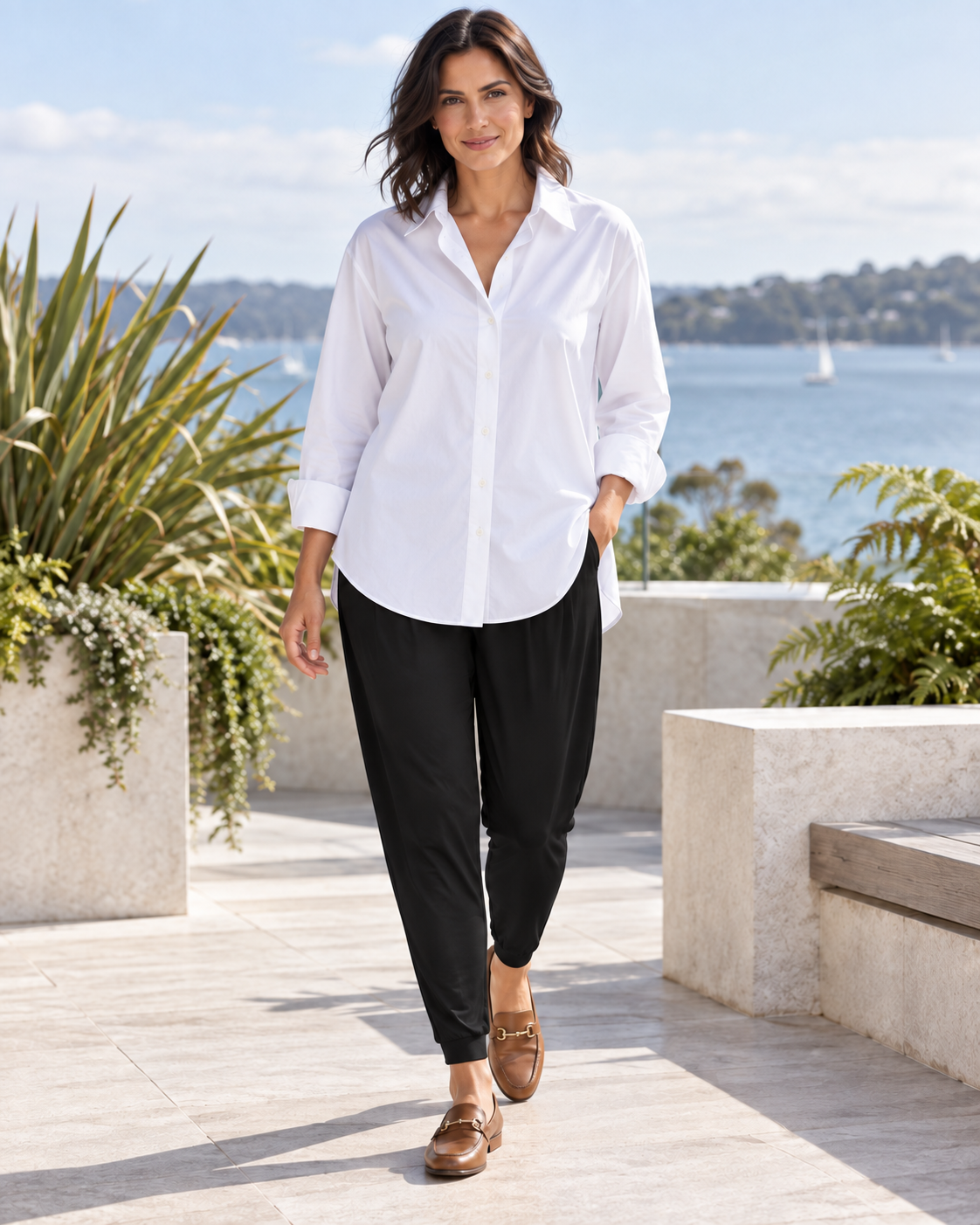 Woman wearing black Paula Ryan Basque pants, an untucked white collared shirt and cognac loafers on a harbour terrace