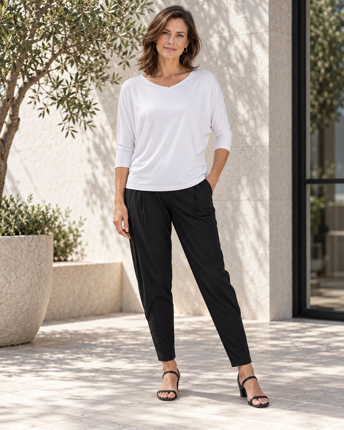 White Classic Batwing Top with relaxed black pants on a sunlit terrace.